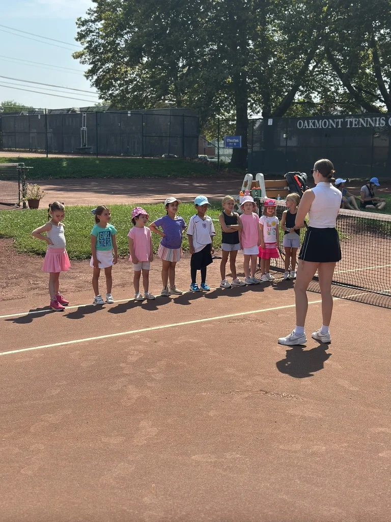 Young junior tennis players lined up with their coach on the red clay courts at Oakmont Tennis Club
